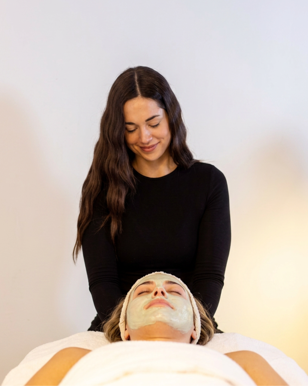 Gena standing behind a client wearing a calming facial mask at Glo Haus